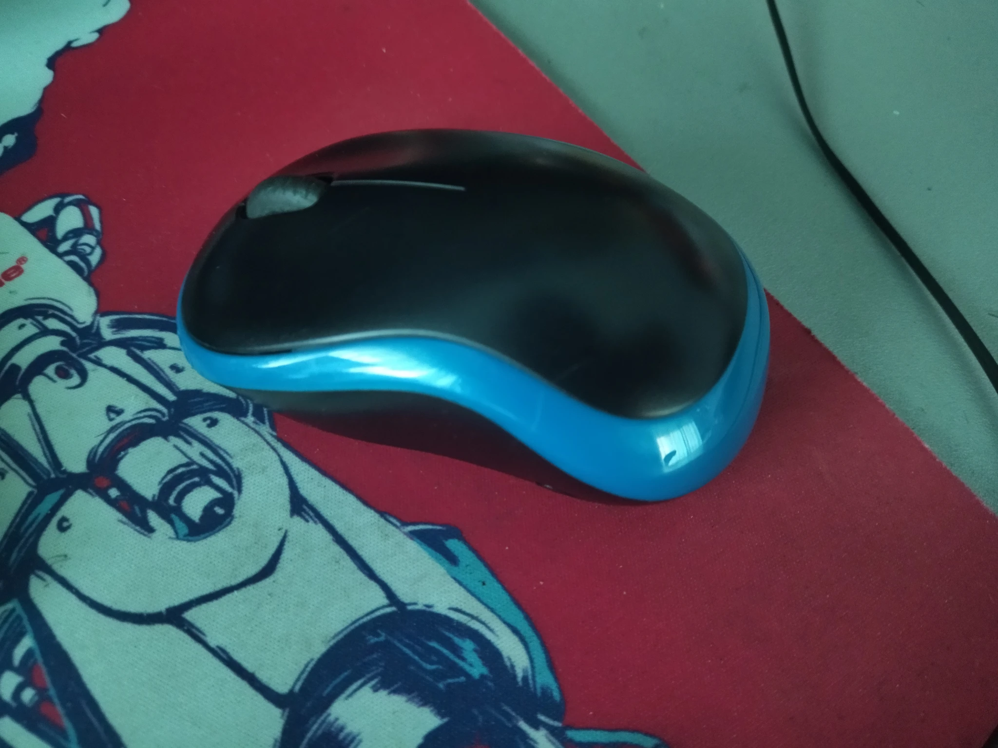 Foto del mouse Logitech piccolino wireless blu e nero, di cui non ricordo il nome di modello, sul mio tappetino, visto ad angolazione obliqua.